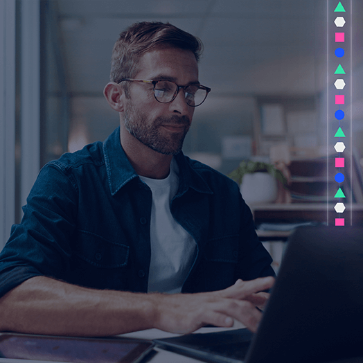 A man wearing glasses and a denim shirt works on a laptop at a desk, likely using ProjectVizion; a vertical row of colorful geometric shapes appears on the right side of the image.